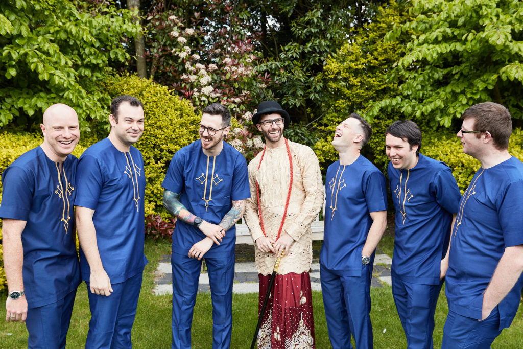 Groomsmen in blue standing either side of the groom in traditional dress