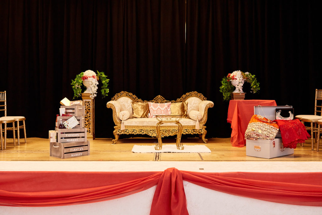Stage set with a gold sofa, flowers and red drapes for the traditional wedding