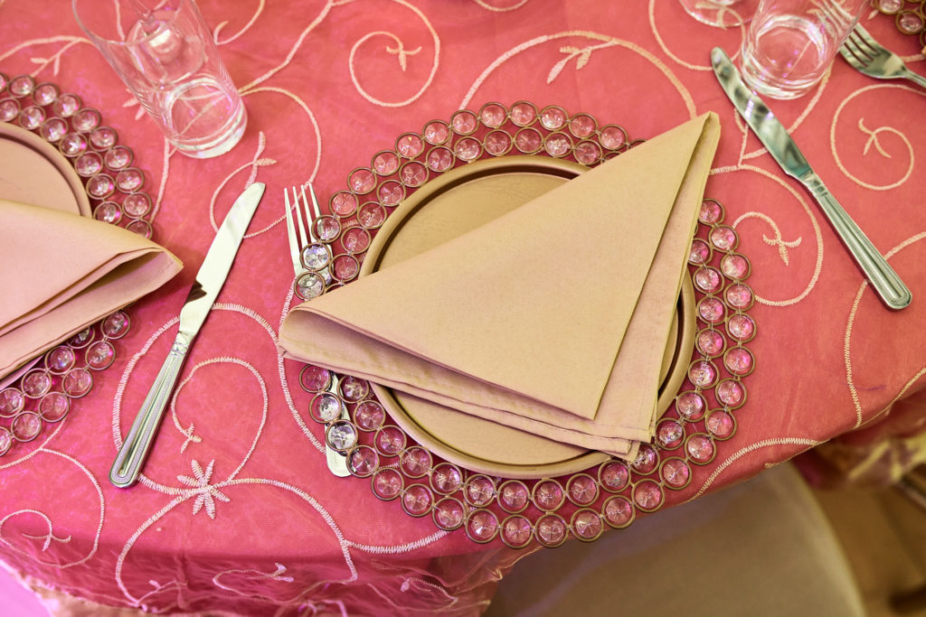 Gold napkin on a beaded charger plate on a pink tablecloth