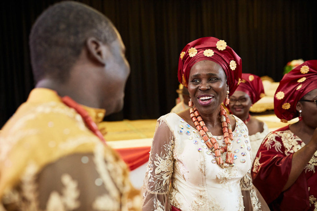 Older woman in a red head tie and coral beads smiling
