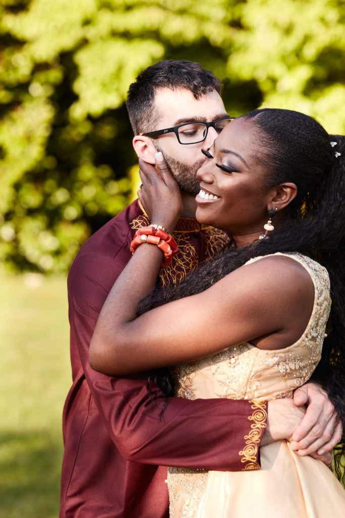 Groom kissing the bride's cheek as she holds his face, in golden evening light