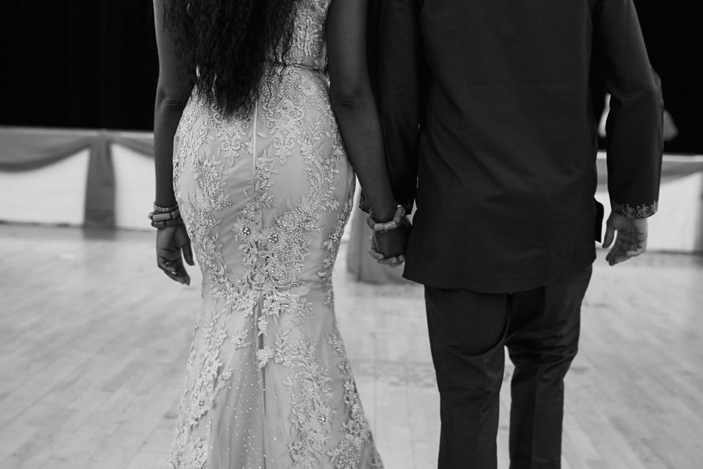 Black and white photo of the bride and groom walking hand in hand, seen from behind