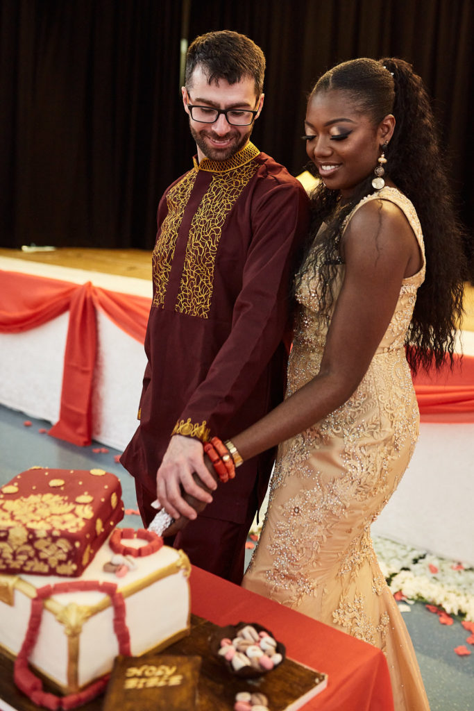 Bride and groom cutting their wedding cake in gold and burgundy outfits