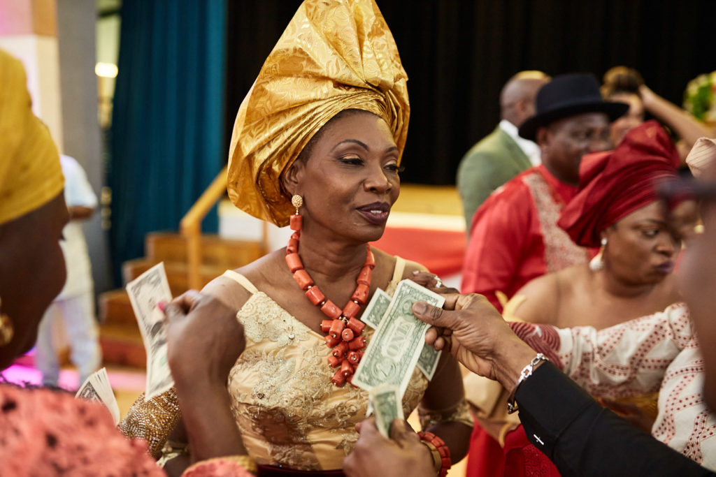 Bride in a gold gele dancing as guests spray her with money