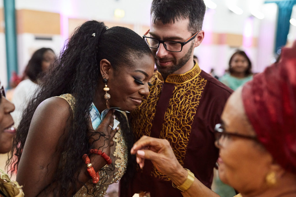 Guests pressing banknotes on the dancing bride as the groom looks on