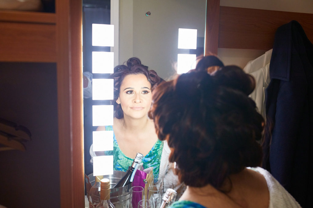Bride with her hair in curls smiling in the mirror as she gets ready