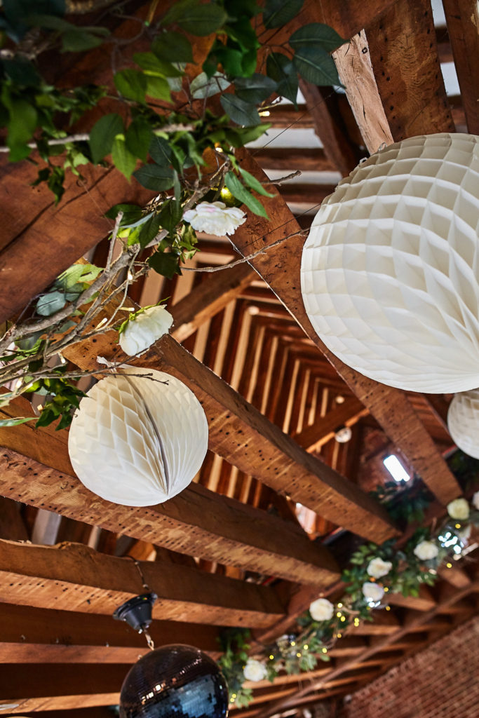 White paper lanterns and flower garlands hanging from the oak beams at Eltham Tudor Barn