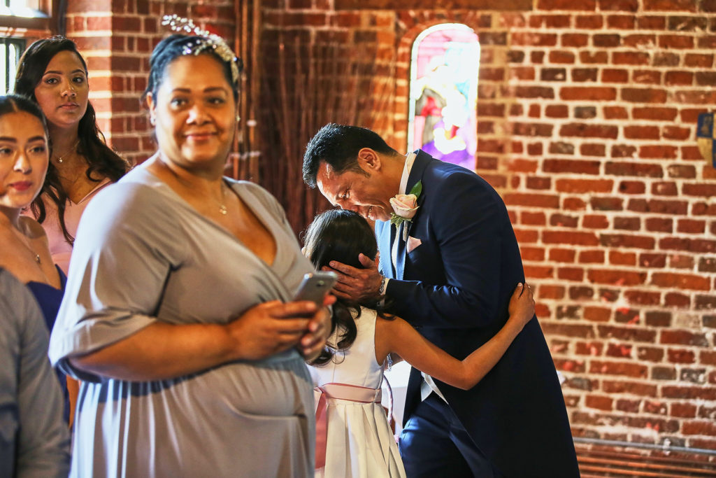 Groom hugging a young bridesmaid as guests look on
