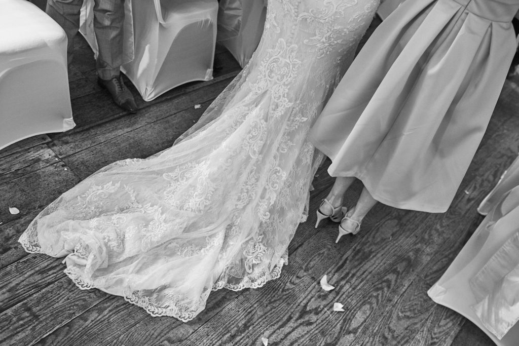 Black and white close-up of the lace train of the wedding dress on the wooden floor