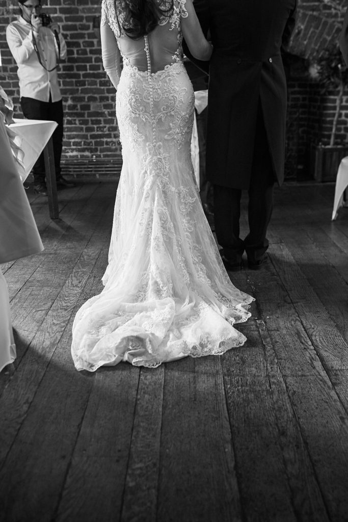 Black and white photo of the bride's lace dress and train from behind during the ceremony