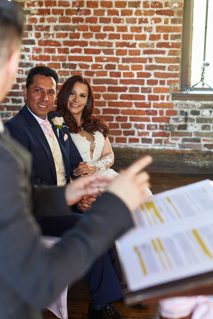 Bride and groom smiling as they listen to a reading during the ceremony