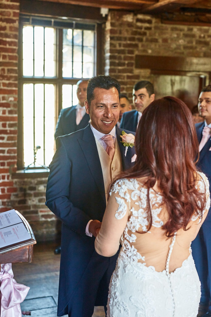 Groom smiling at the bride during their wedding ceremony at Eltham Tudor Barn