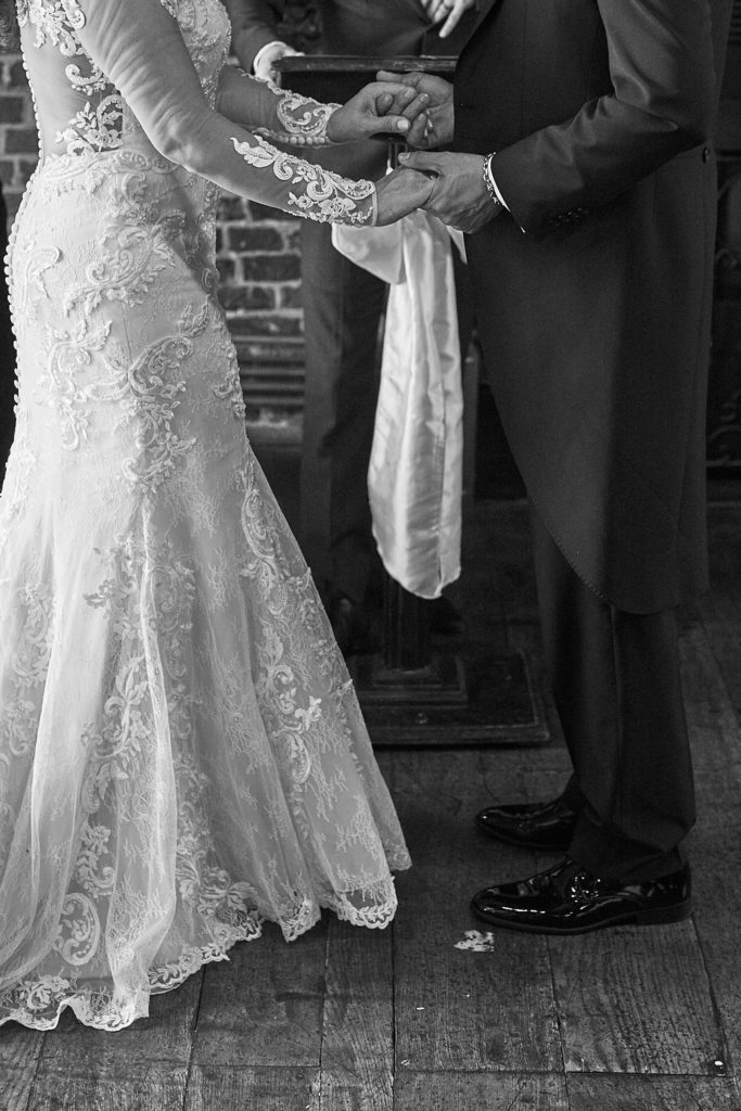 Black and white photo of the bride and groom holding hands during their vows