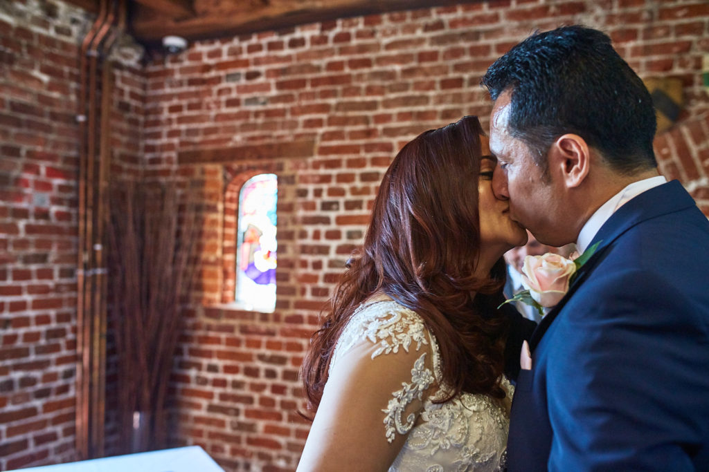 Bride and groom's first kiss in front of a red-brick wall at Eltham Tudor Barn