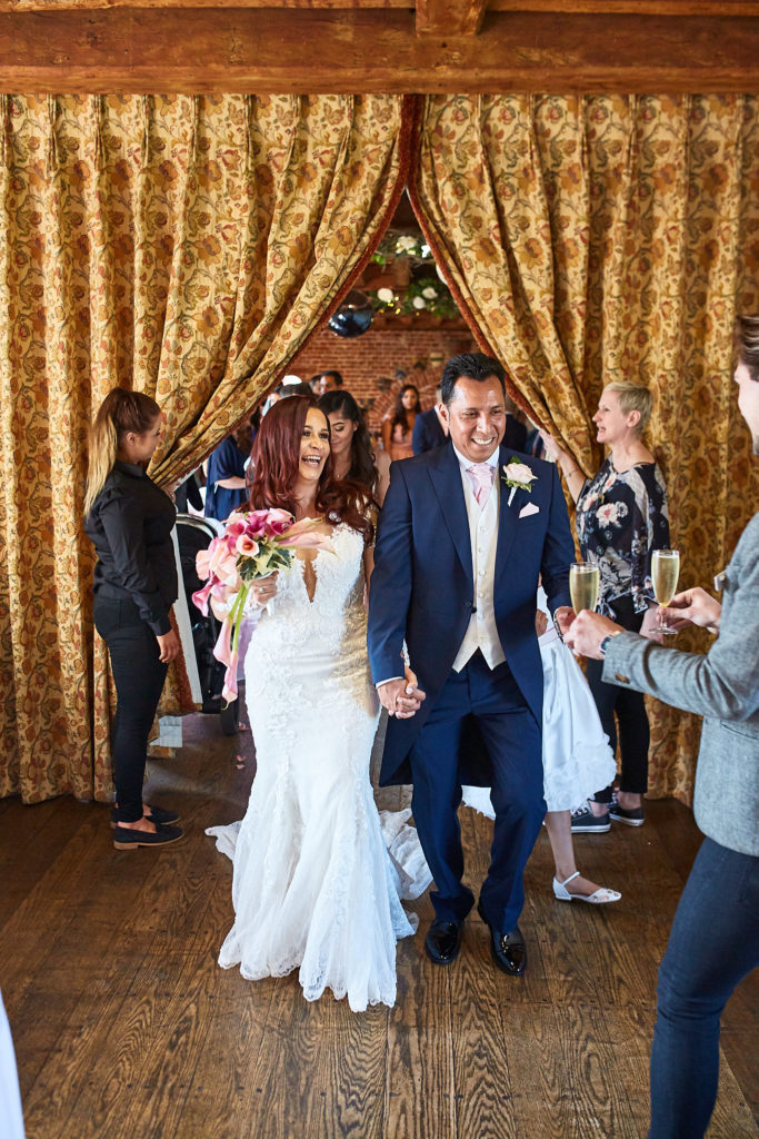 Bride and groom walking out through gold curtains as guests applaud