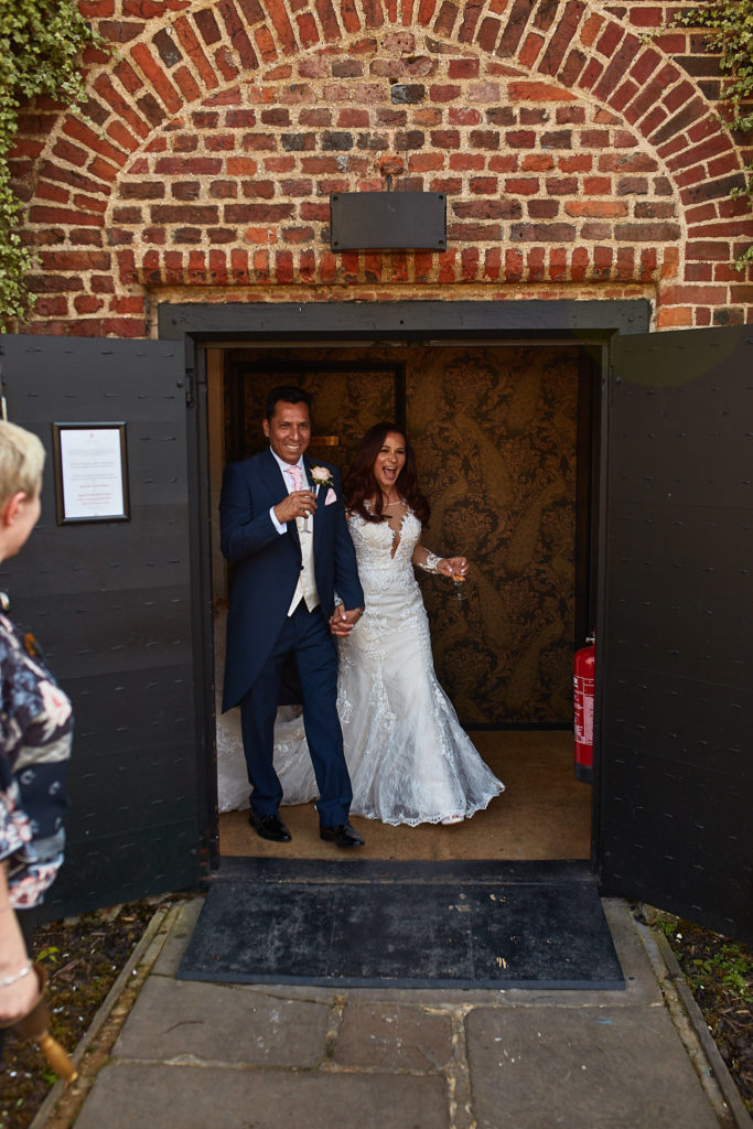 Bride and groom laughing as they walk out through the doorway at Eltham Tudor Barn