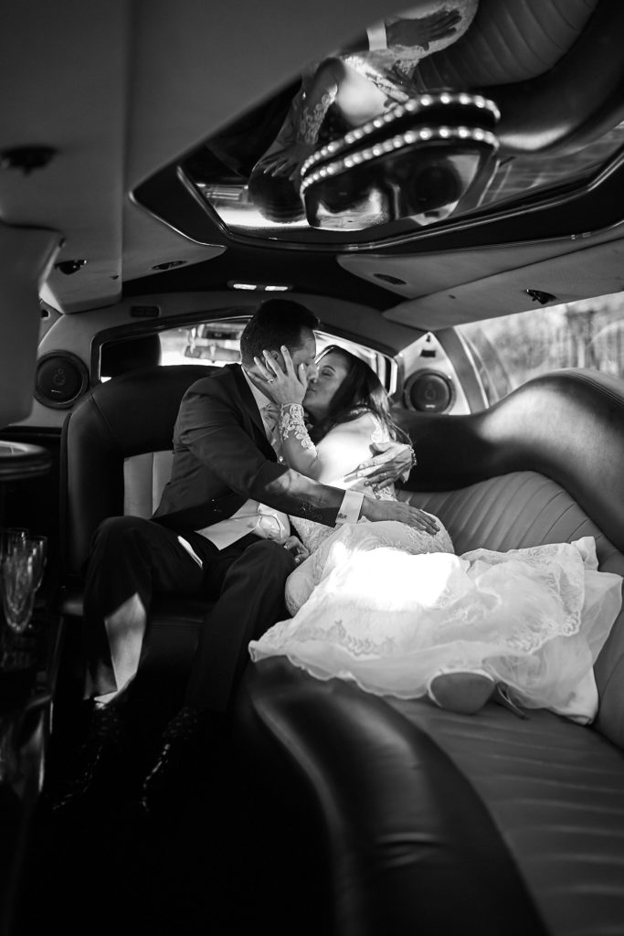 Black and white photo of the bride and groom kissing inside the limousine