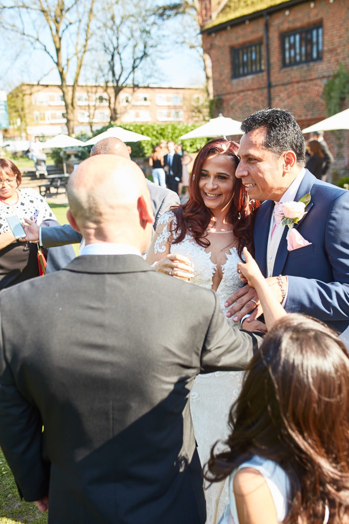 Bride and groom greeting guests in the garden at Eltham Tudor Barn