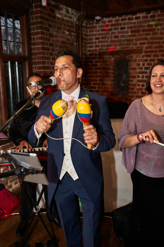 Groom singing into a microphone while playing maracas with the band