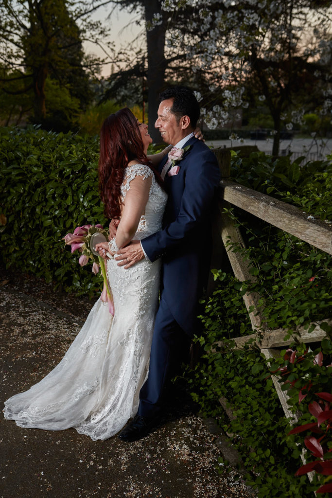 Bride and groom embracing in the gardens at Eltham Tudor Barn in the evening