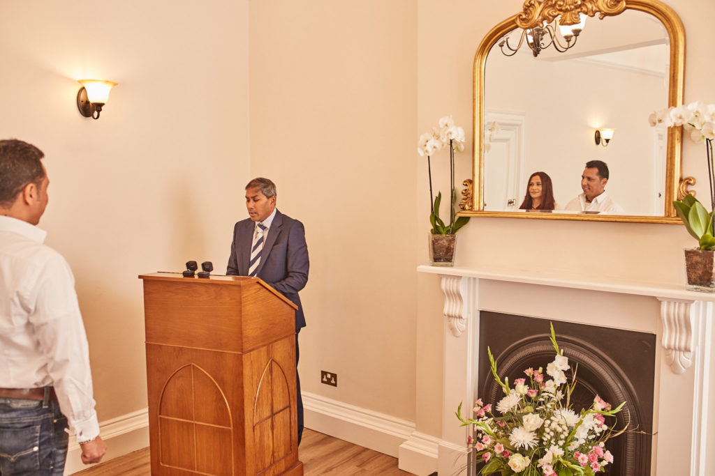 Registrar standing at the lectern beside a fireplace and gilt mirror
