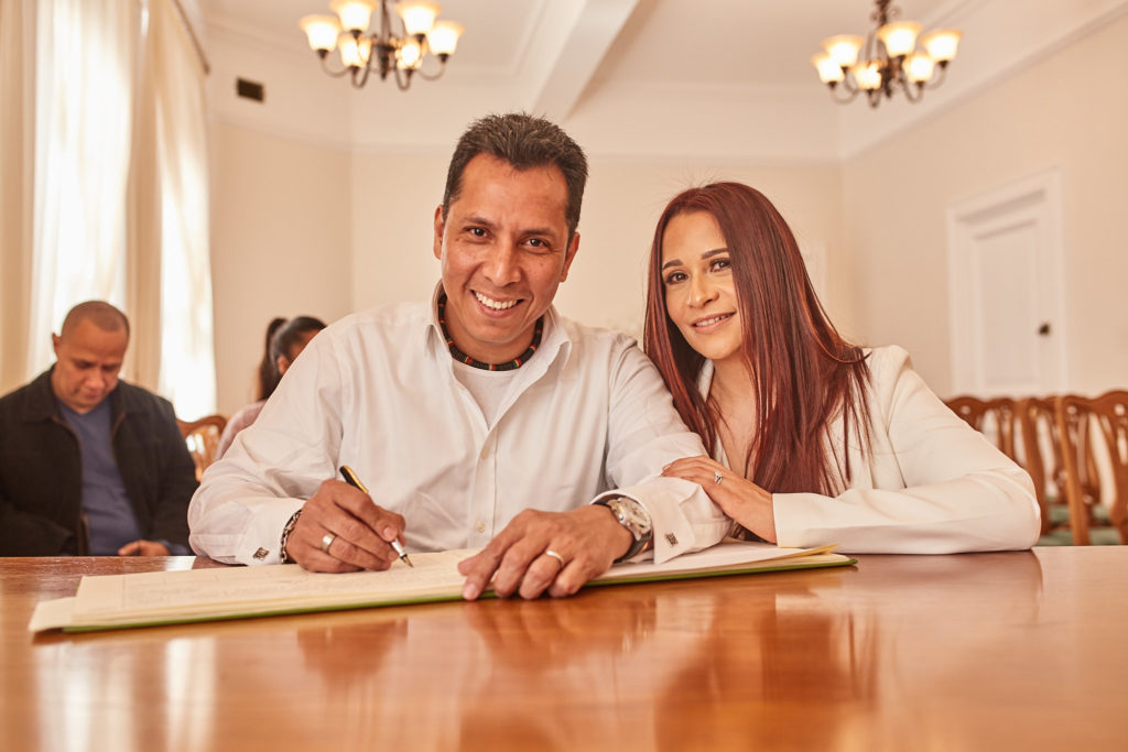 Bride and groom smiling as they sign the register at Woolwich Town Hall