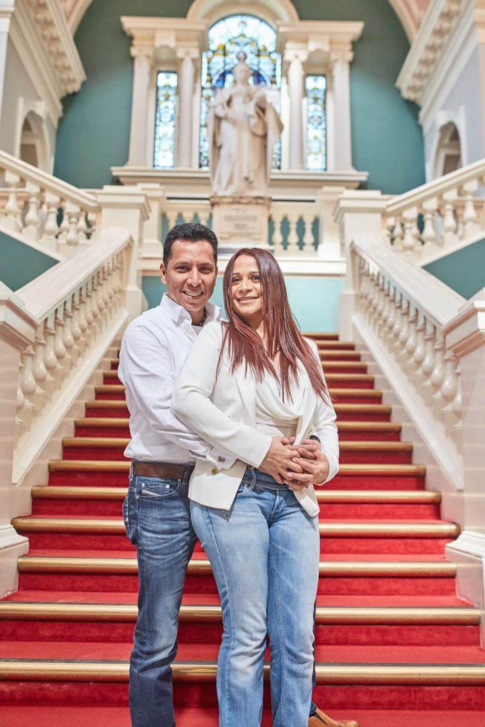 Groom hugging the bride from behind on the red-carpeted staircase at Woolwich Town Hall