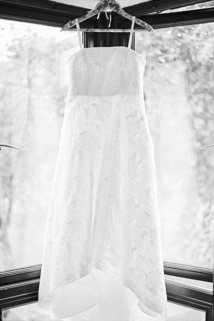Black and white photo of the wedding dress hanging in a bay window