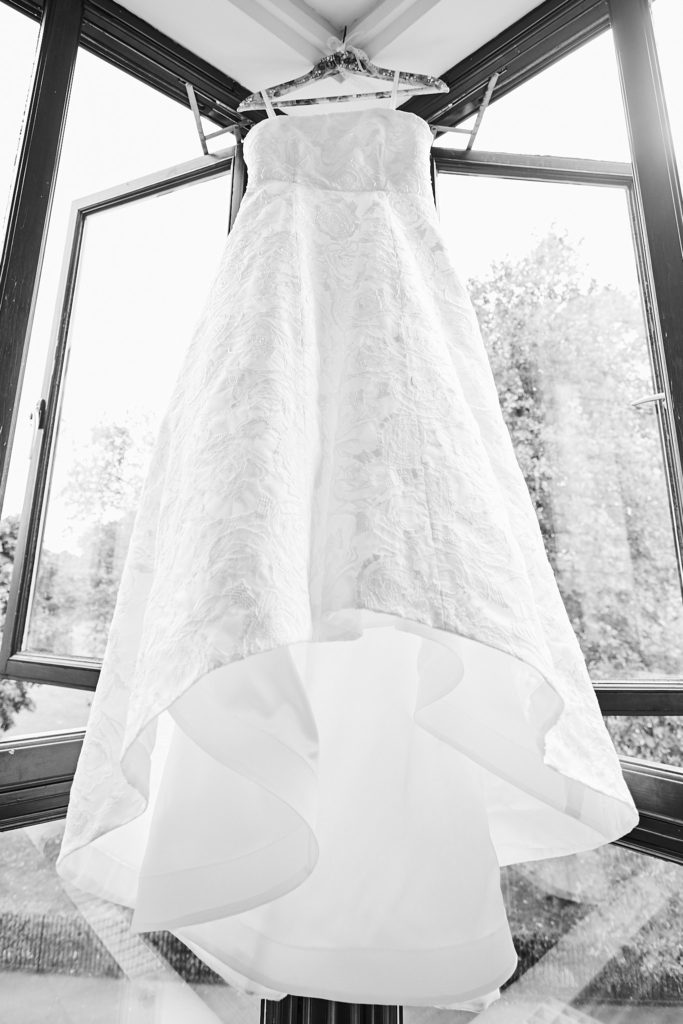 Black and white photo of the wedding dress and its train hanging in a window