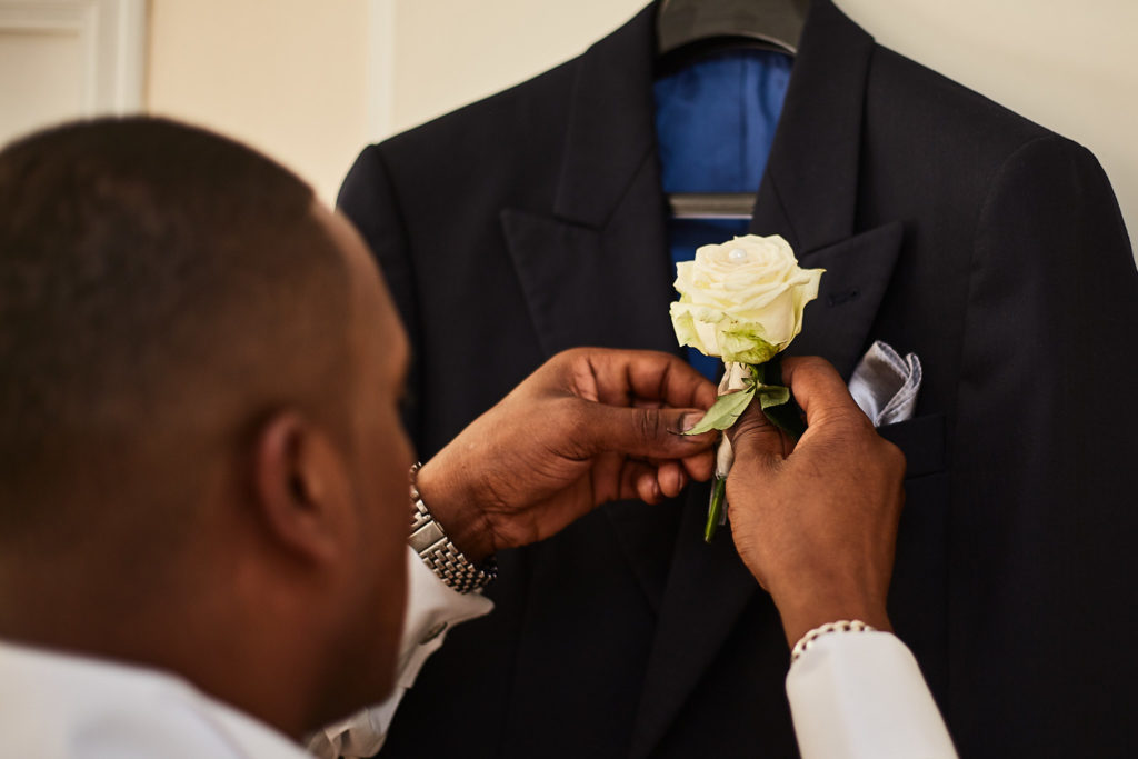 Groomsman pinning a cream rose buttonhole on a suit jacket