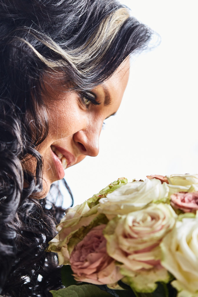 Bride with curled hair looking down at her bouquet of cream and pink roses