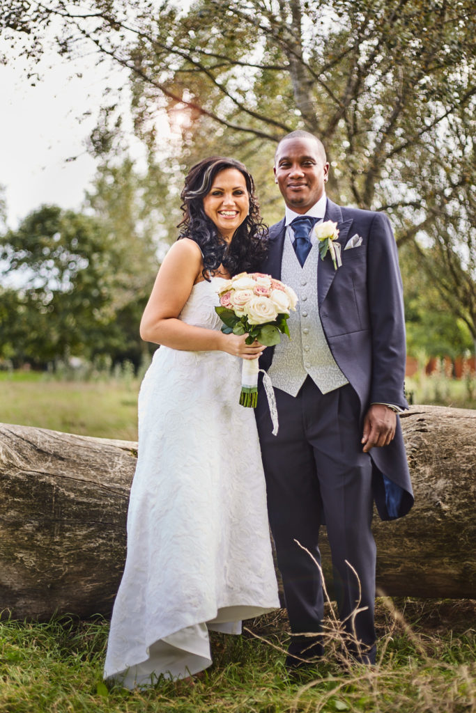Bride and groom laughing together beside a fallen tree in the park