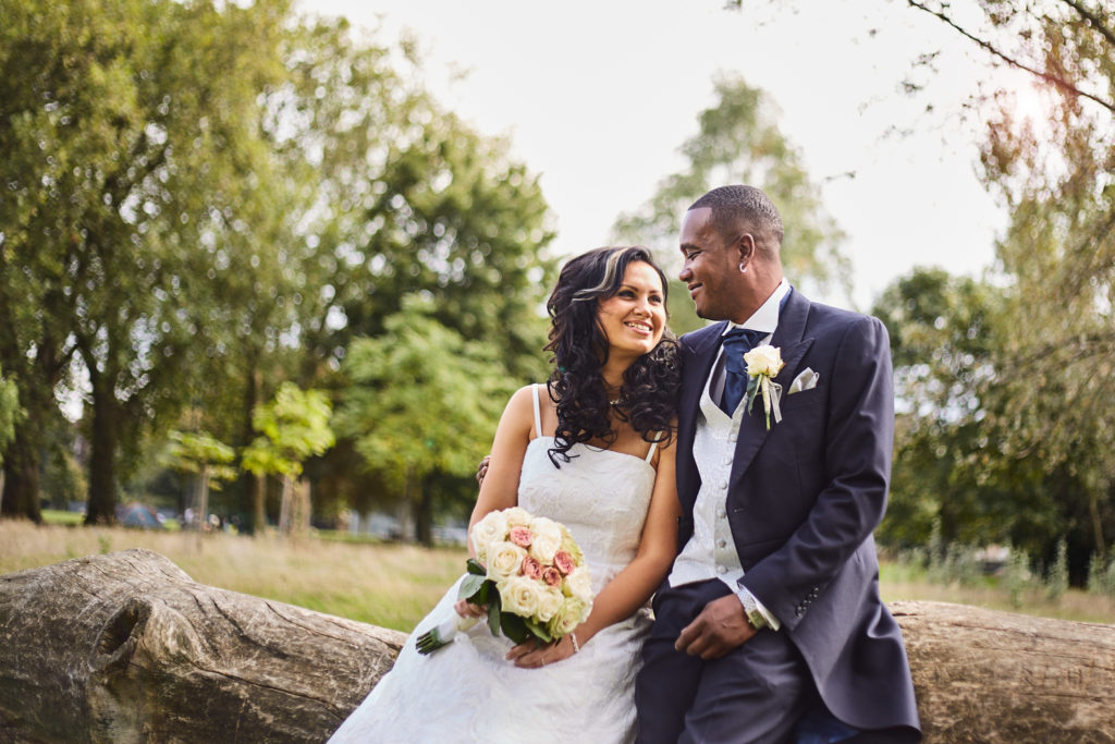 Bride and groom sitting on a log in the park, smiling at each other