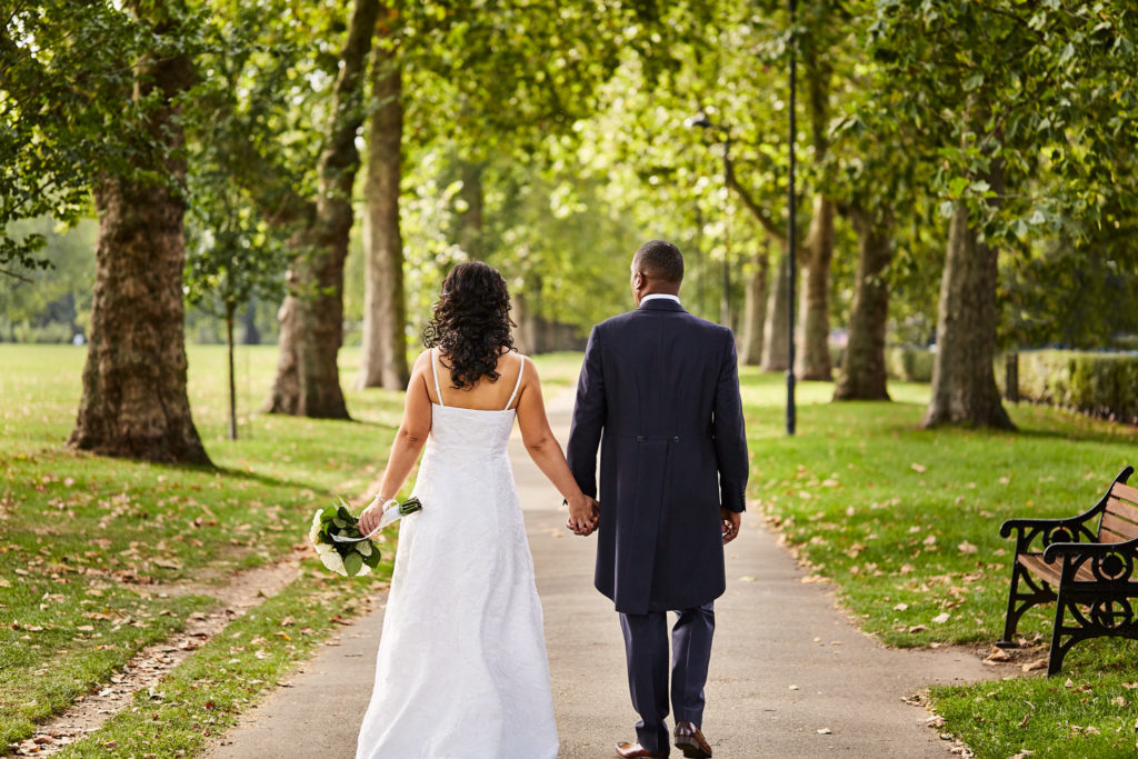Bride and groom walking hand in hand along a tree-lined path, seen from behind
