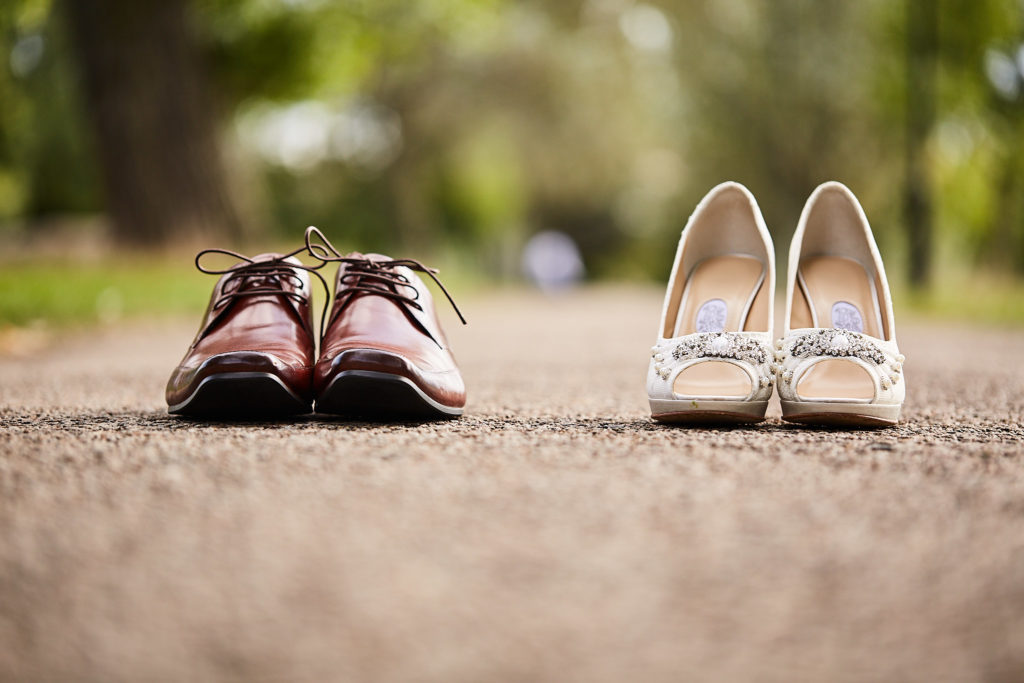 Groom's burgundy brogues and the bride's ivory shoes on a park path