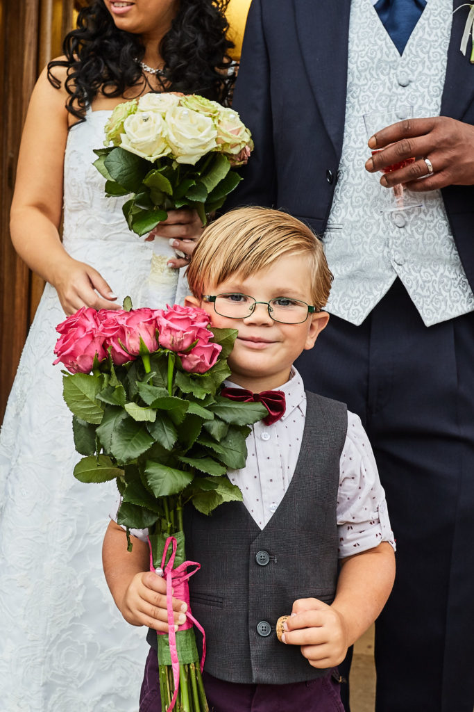 Young page boy in glasses and a bow tie holding a bunch of pink roses