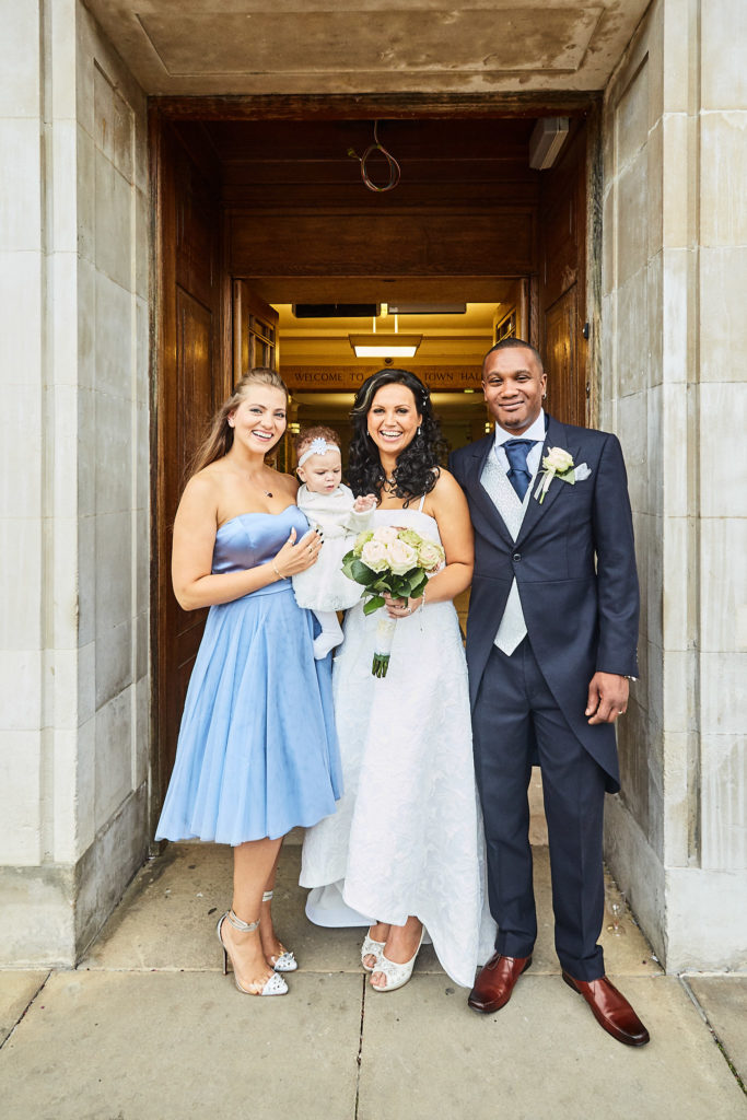 Bride and groom in a stone doorway with a guest holding a baby