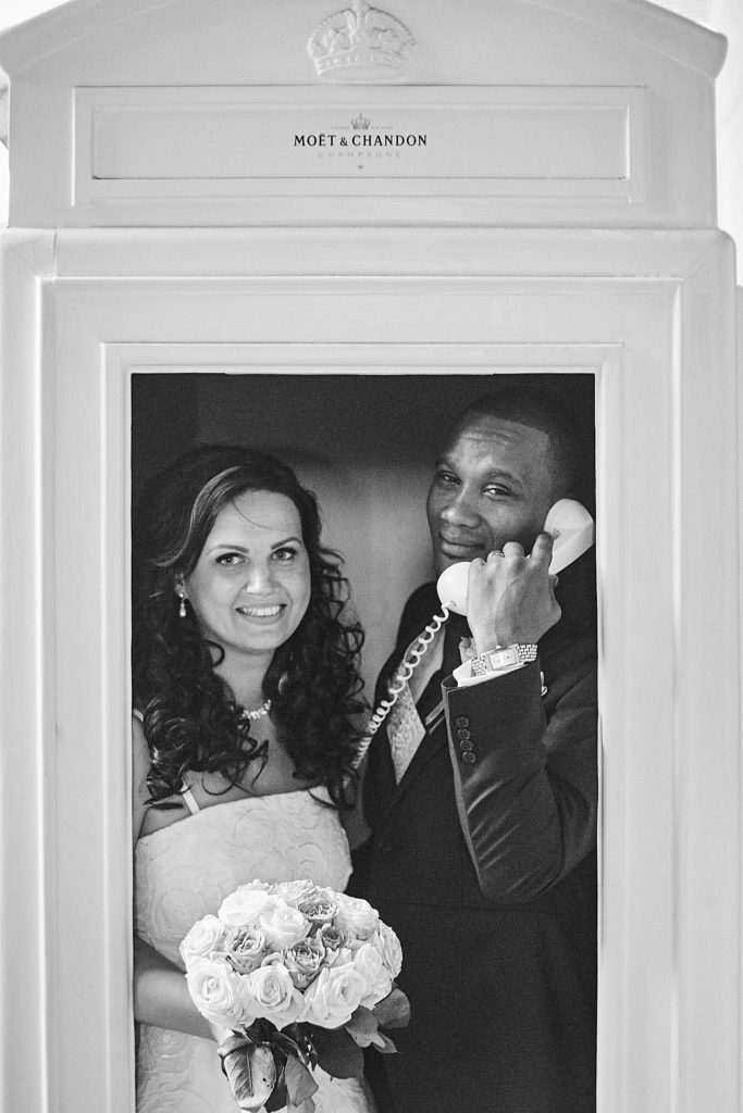 Black and white photo of the bride and groom squeezed into a telephone box, the groom on the phone