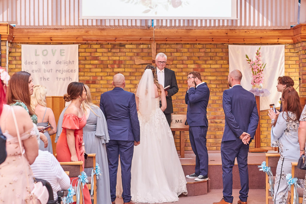 Wedding ceremony in a brick-walled church with the bridal party standing at the front