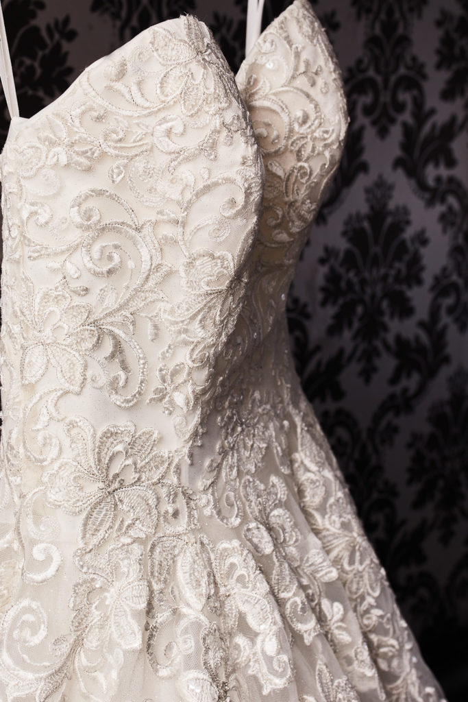 Embroidered lace wedding dress hanging against patterned wallpaper