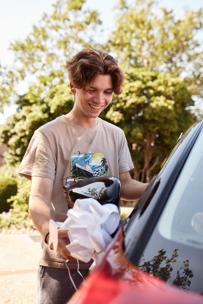 Young man laughing as he decorates the wedding car