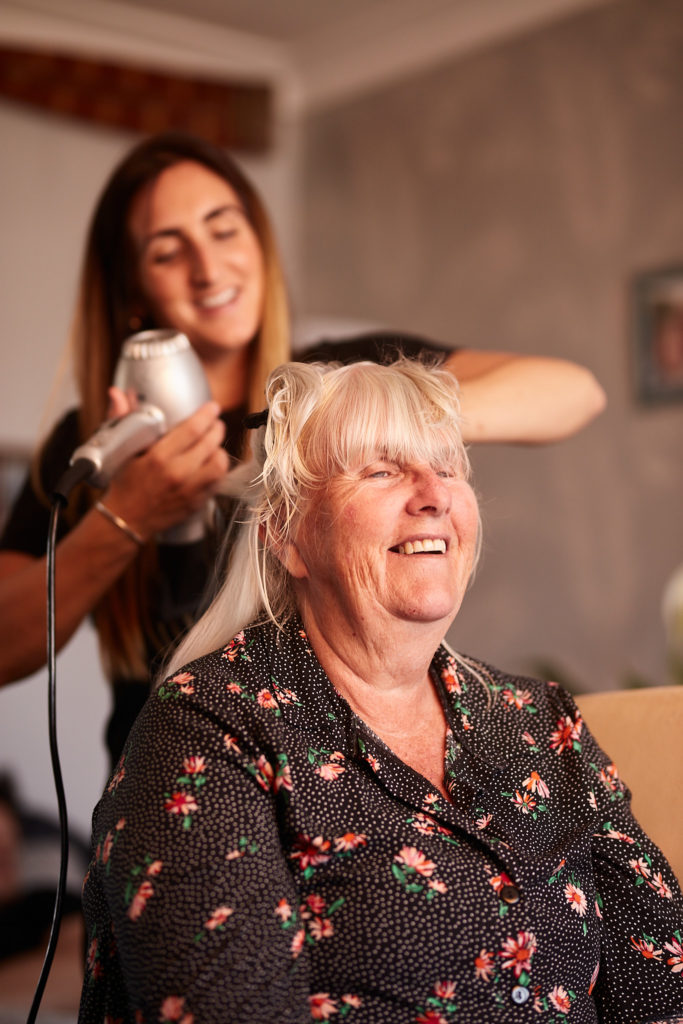 Older woman laughing as her hair is blow-dried