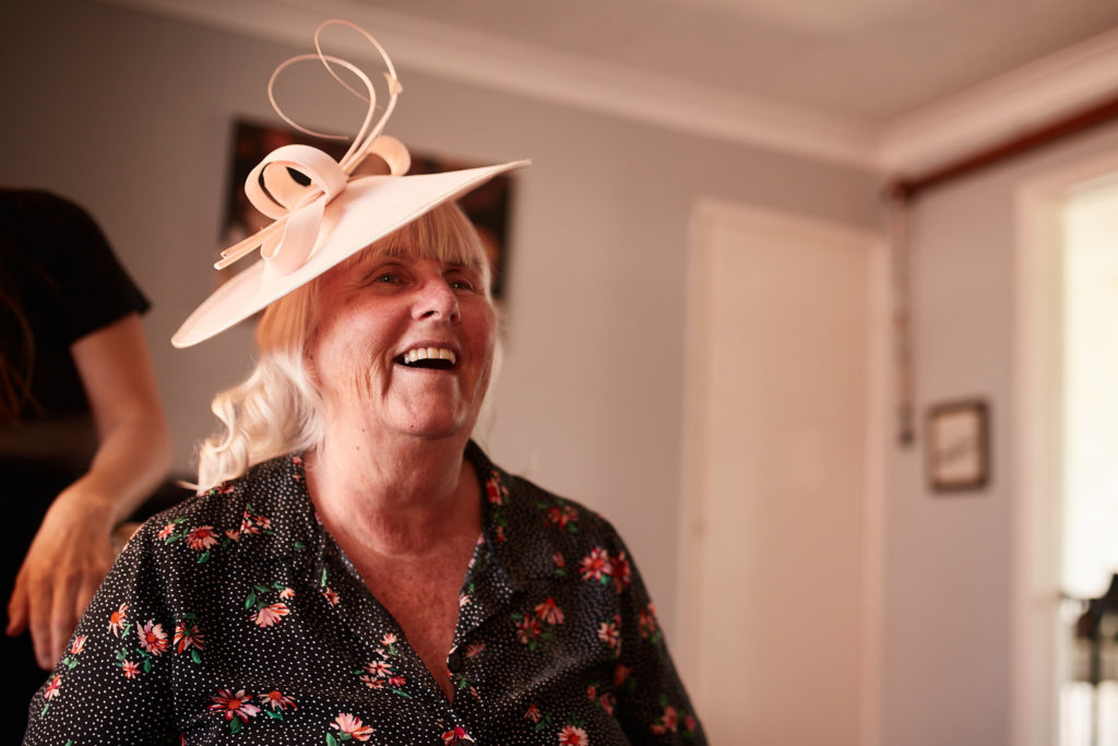 Woman in a cream fascinator laughing on the wedding morning