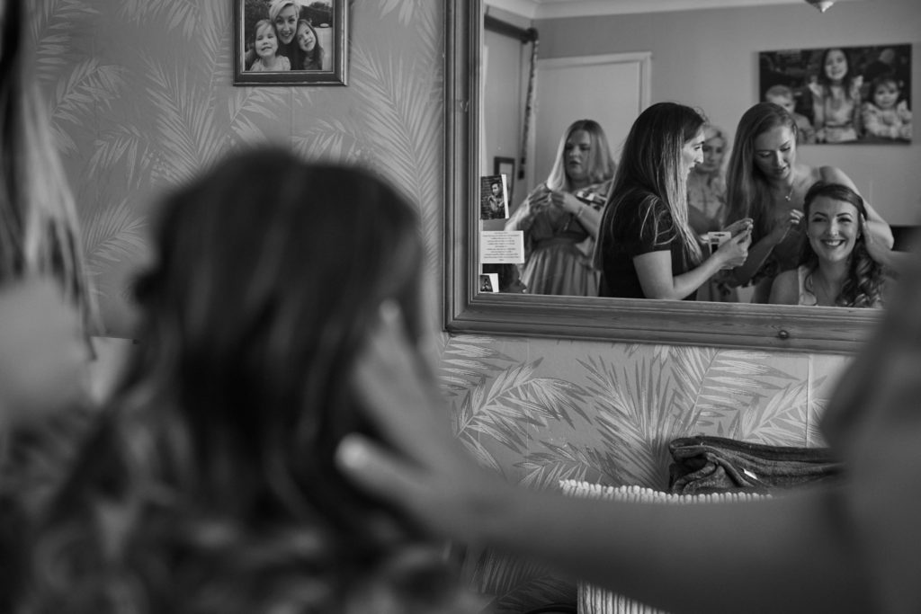 Black and white photo of bridesmaids getting ready, reflected in a mirror