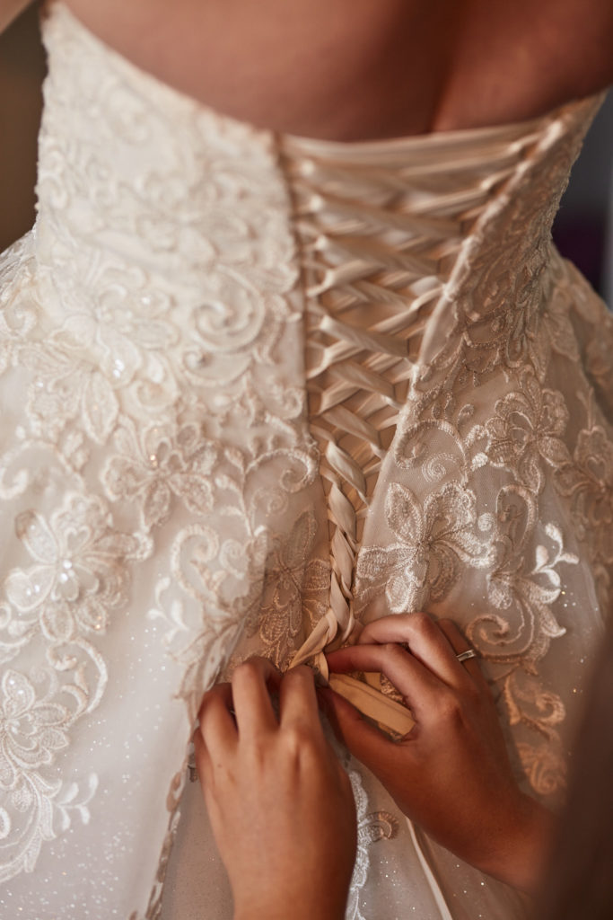 Close-up of hands tying the ribbon lacing on the back of the lace wedding dress