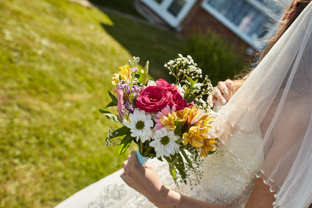Bride holding her bouquet of pink and yellow flowers outside in the sunshine