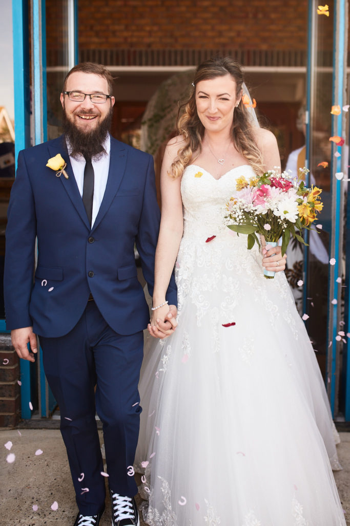 Bride and groom leaving the church as confetti falls, the groom in Converse trainers