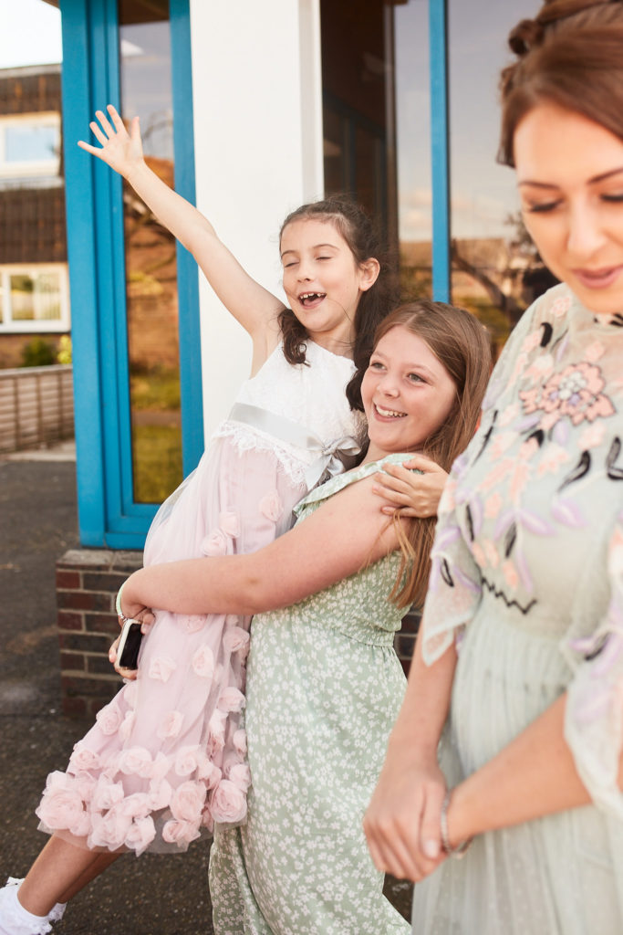 Young bridesmaids hugging and waving outside the church