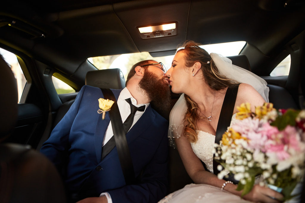 Bride and groom kissing in the back of the wedding car