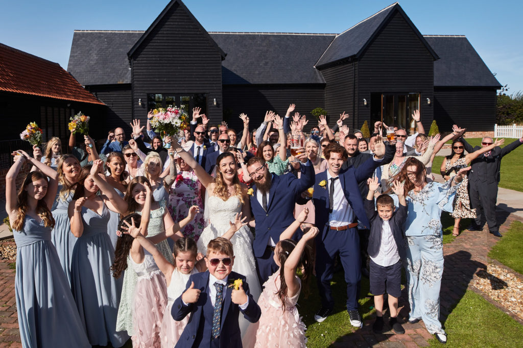 Group photo of all the wedding guests waving in front of Villiers Barn